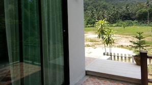 A room with a sliding glass door leading to a balcony with a view of a lush landscape and a mountain in the distance. - The Tree Madauwan (Ko Pha-ngan)