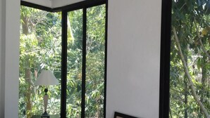 A room with a large window offering a view of dense greenery. There is a table with a lamp and a chair. - The Tree Madauwan (Ko Pha-ngan)