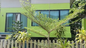 A building with a green facade, a white picket fence, and various plants in the foreground. - The Tree Madauwan (Ko Pha-ngan)