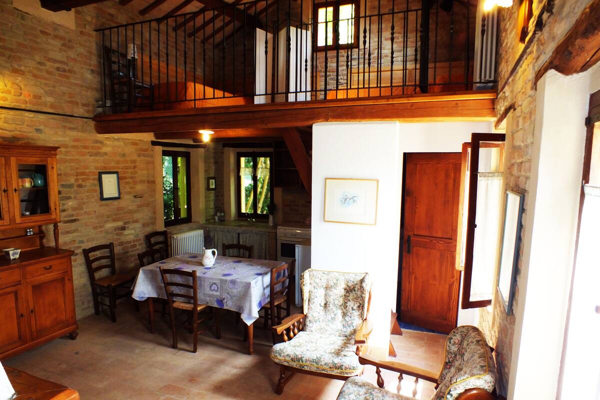 A rustic dining area with a wooden table, chairs, and a view of the outdoors through windows.