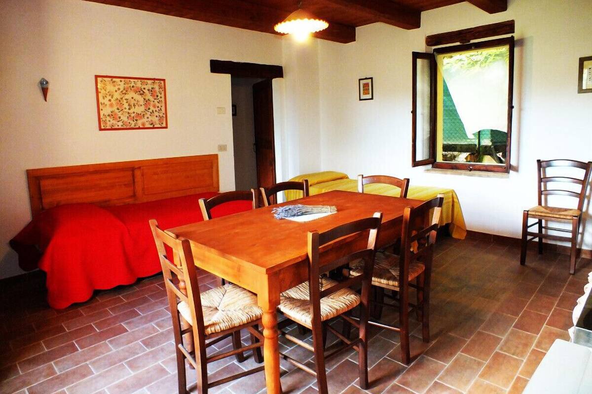 A dining area with a wooden table and chairs, a red sofa, and a window with a view.
