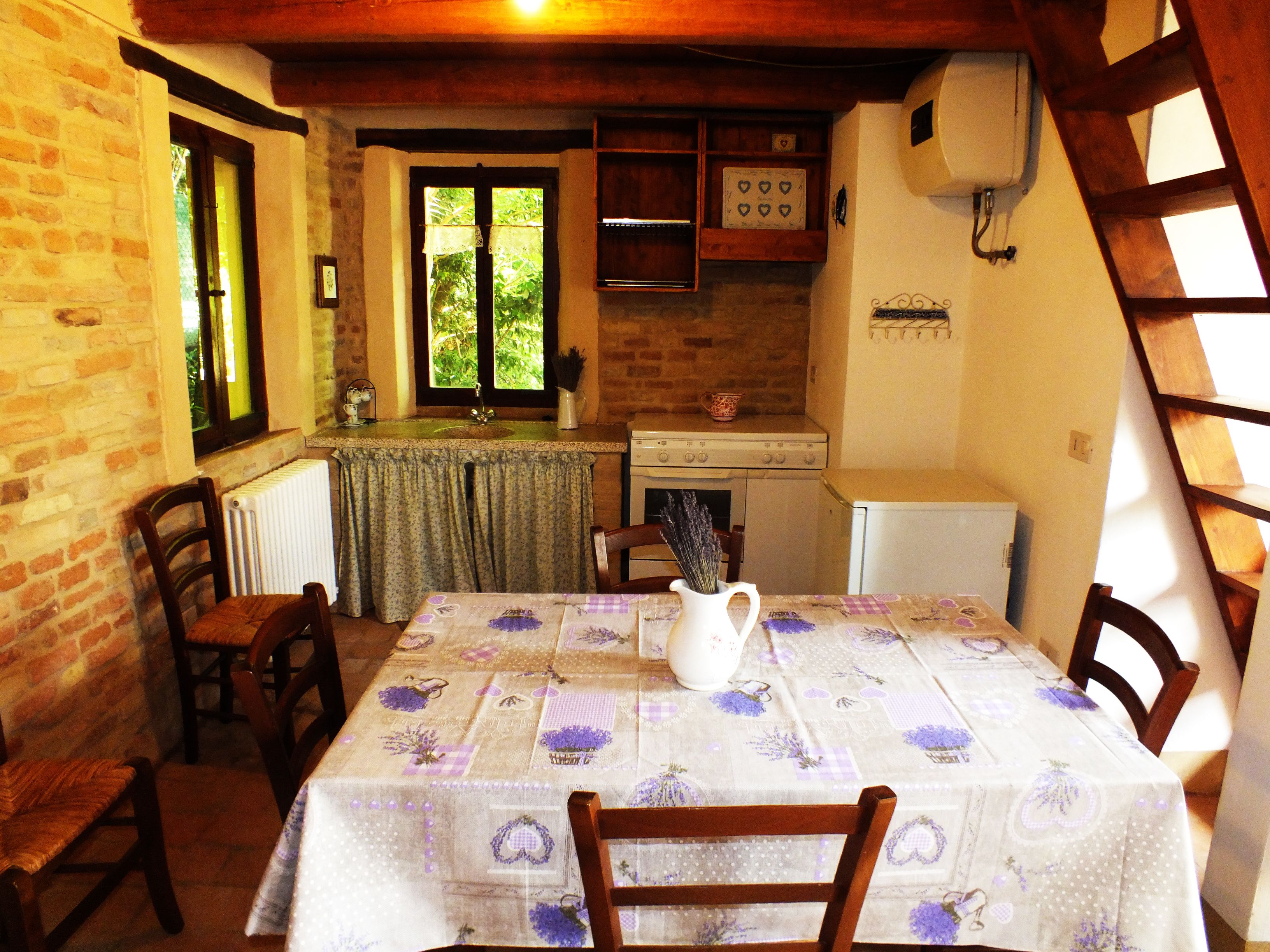 Una cocina rústica con una mesa de madera dispuesta para comer, una ventana con cortinas y un refrigerador blanco.