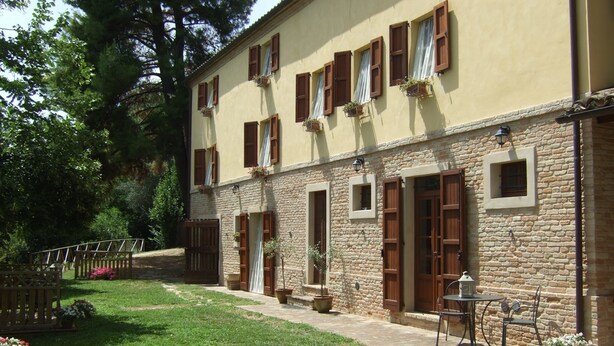 Un bâtiment à deux étages avec des murs en pierre et des volets en bois, une cour pavée avec une pelouse et des sièges extérieurs.