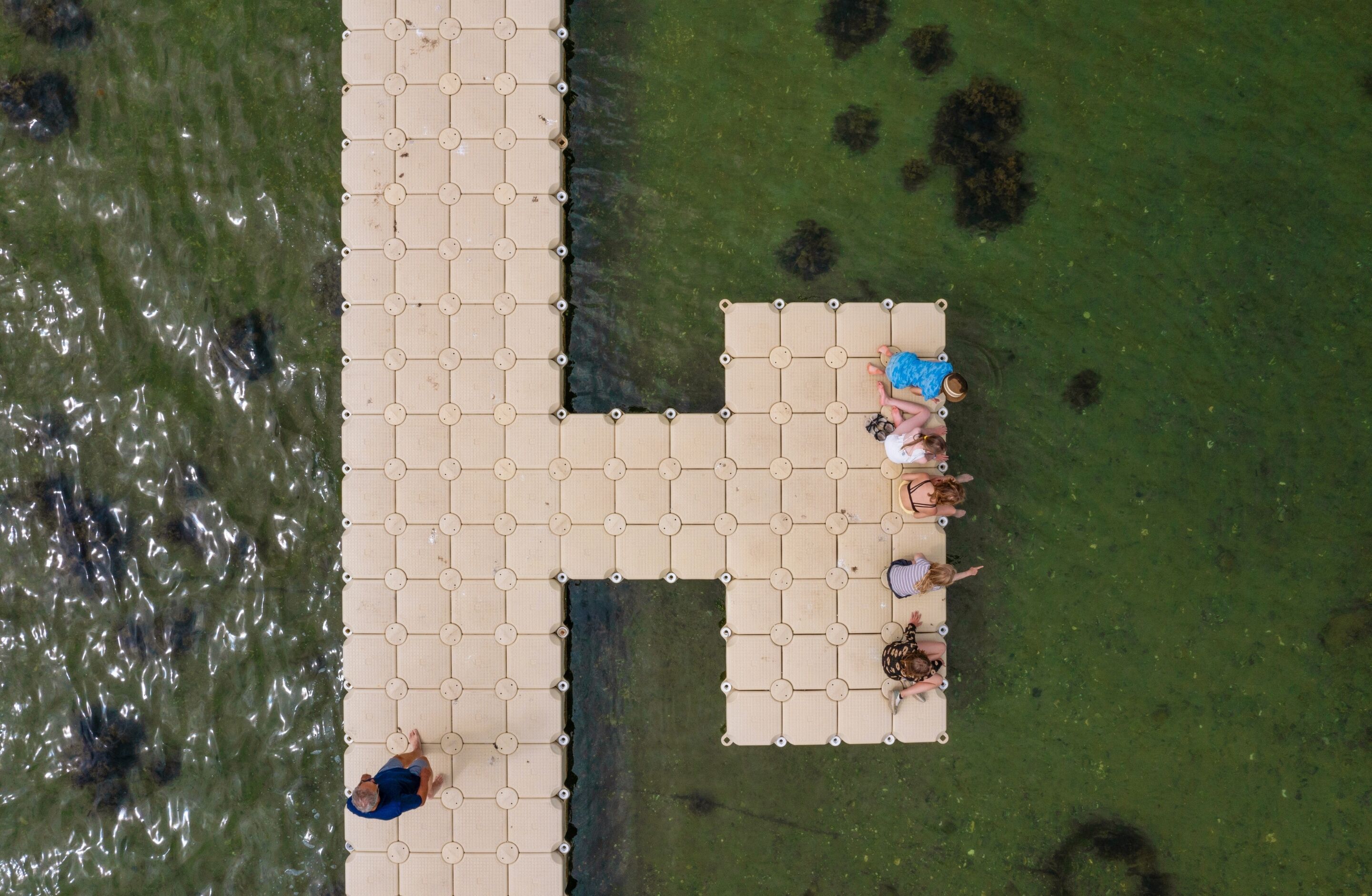 A tiled deck extending into a body of water, with a few people sitting and standing.
