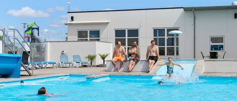 Una piscina con gente sentada en el borde y una persona nadando.