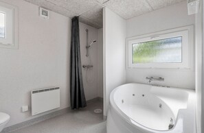 A modern bathroom with a shower, a bathtub, a window with a view, and a radiator. - First Camp Bøjden Strand (Faaborg)