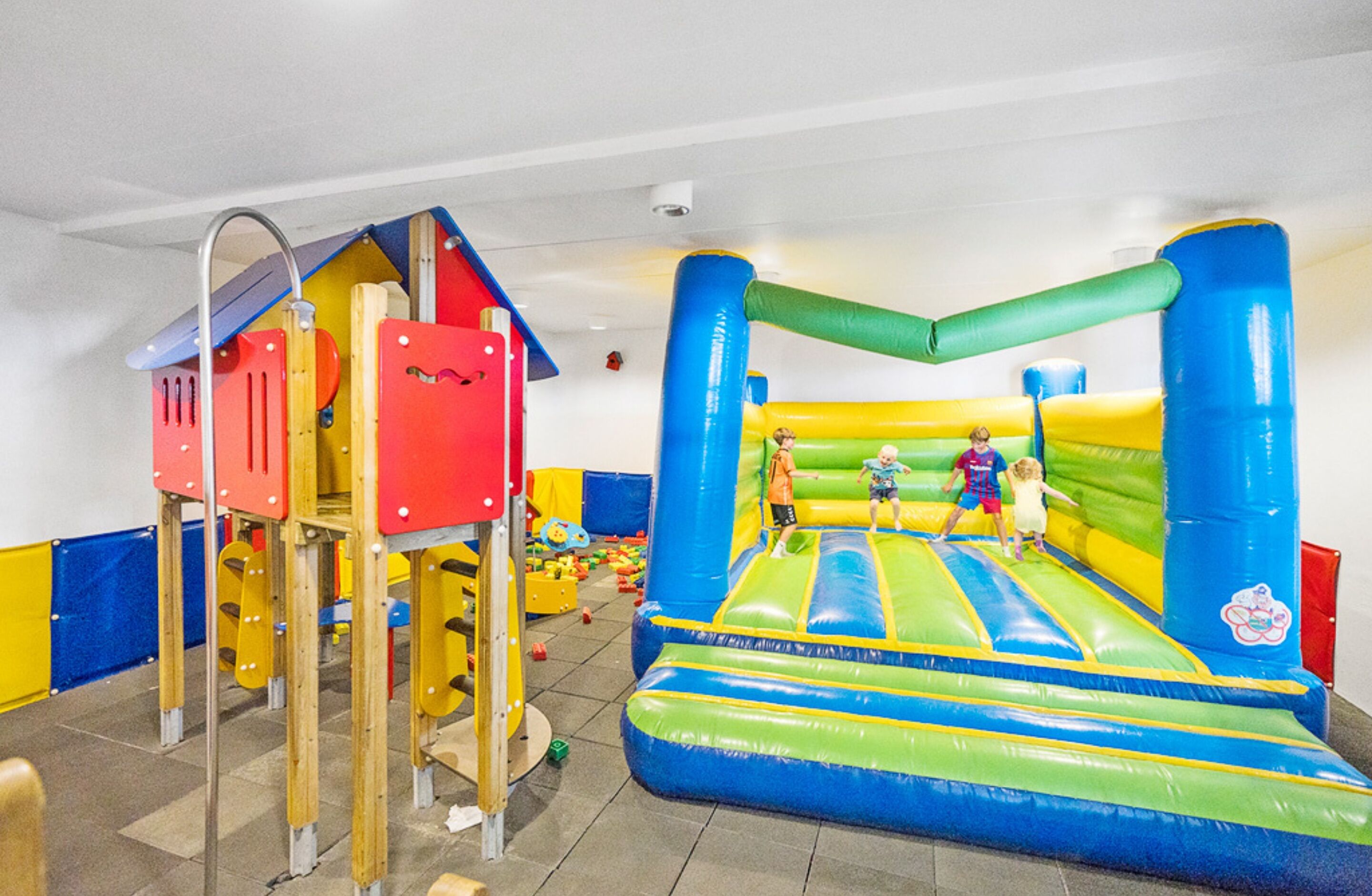 An indoor play area with a colorful play structure and a large inflatable bounce house.