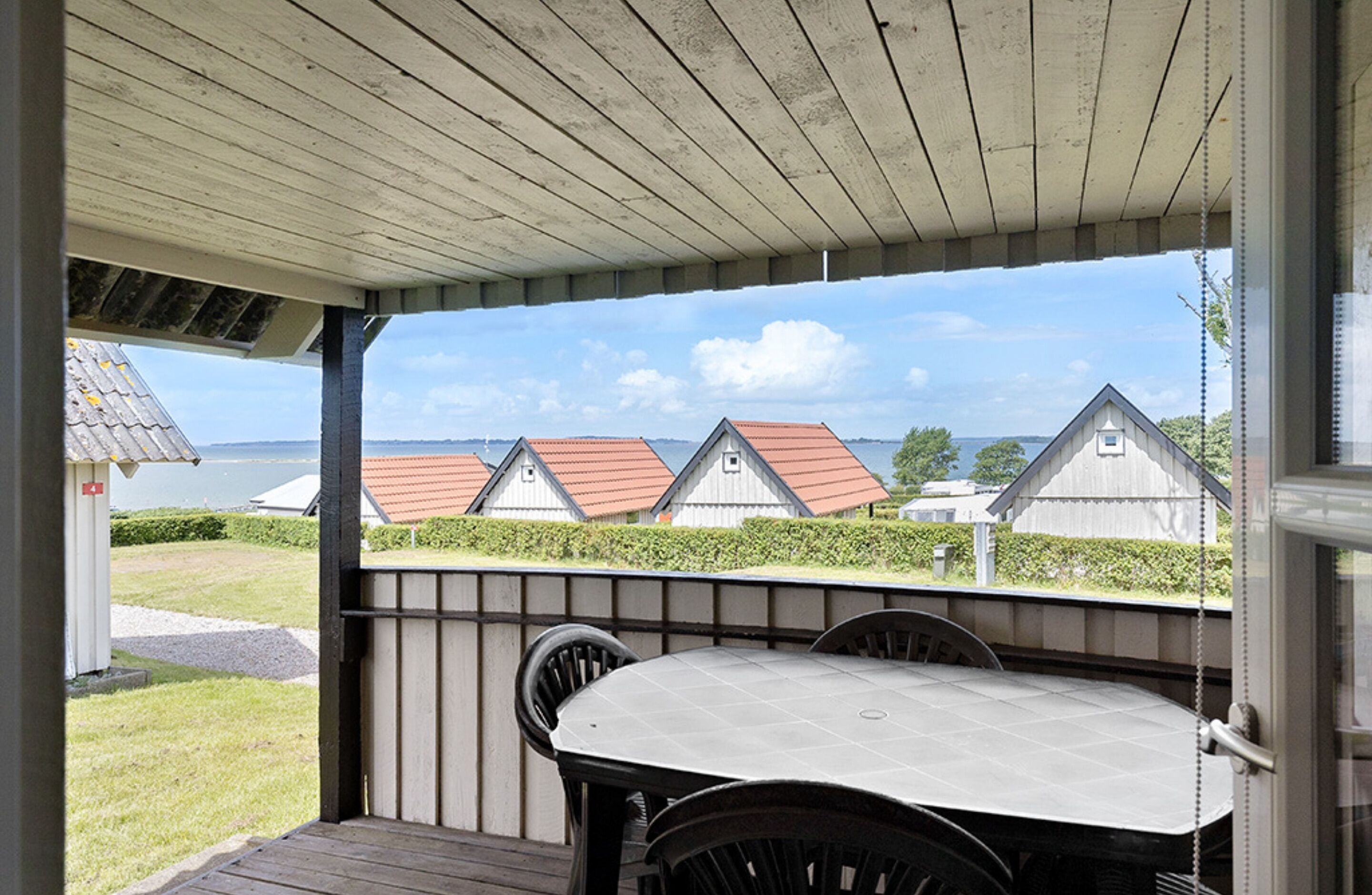 Un patio techado con una mesa y sillas, con vistas a una hilera de casas con tejados rojos y una masa de agua al fondo.