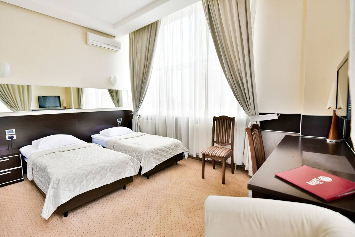 A hotel room with two beds, a desk, a chair, and a large window with curtains.