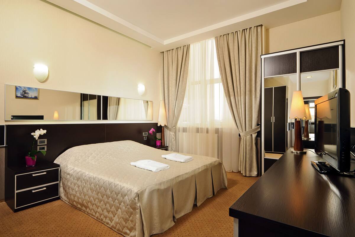 A hotel room with a bed, bedside table, lamp, mirror, and a dresser.