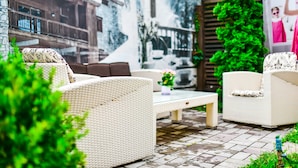Un espace patio aménagé avec des meubles en osier, une table en verre et un mur décoré d’une fresque.