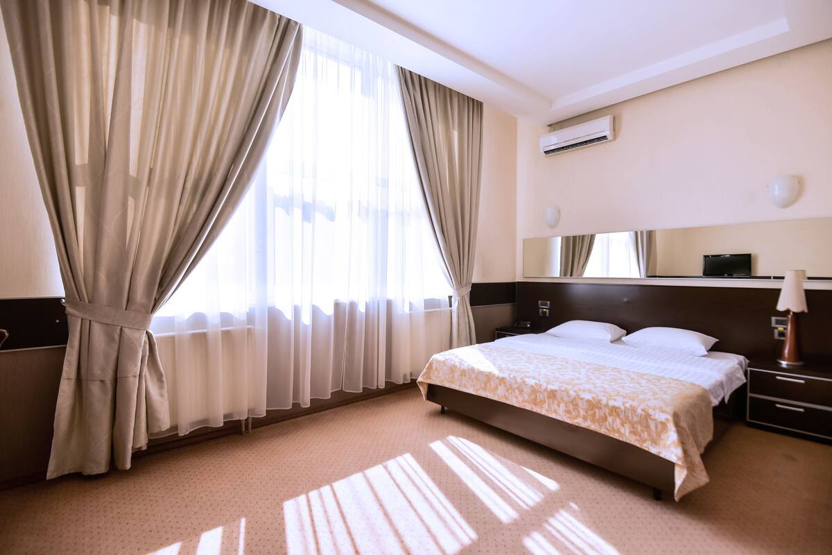 A hotel room with a large bed, a bedside table, a lamp, and a window with curtains.