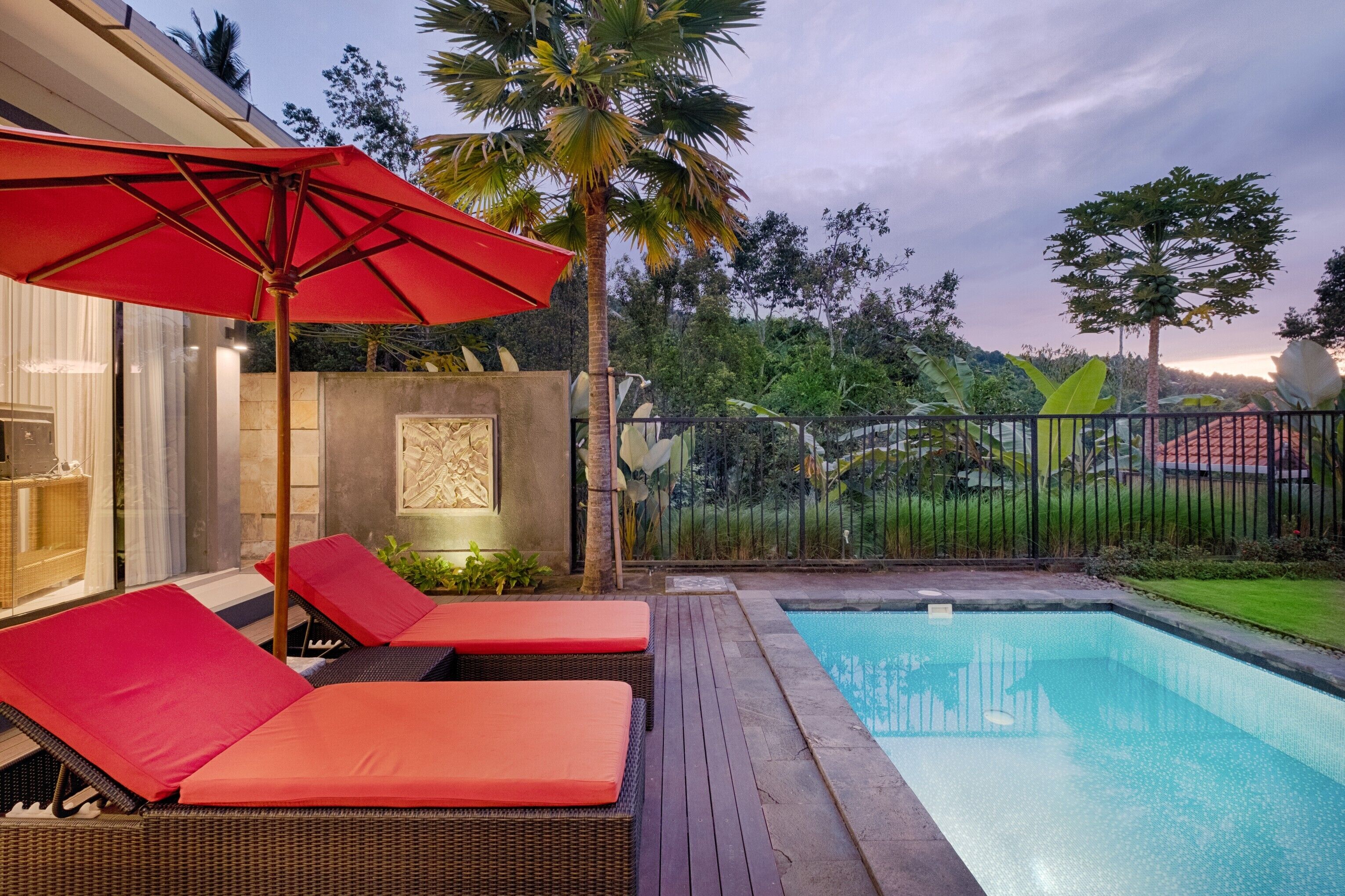 Zona de piscina con sillones de descanso y una sombrilla roja.