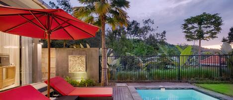 Zona de piscina con sillones de descanso y una sombrilla roja.