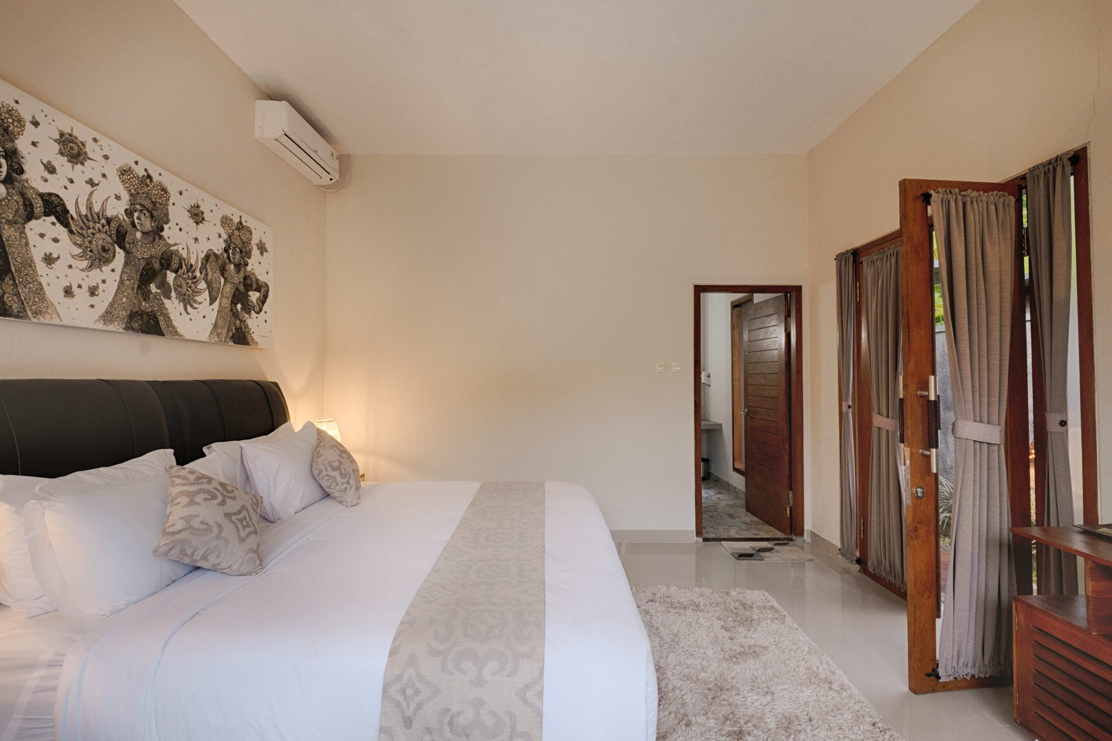 Un dormitorio con una cama grande, cabecera, aire acondicionado instalado en la pared y una puerta que da a otra habitación.