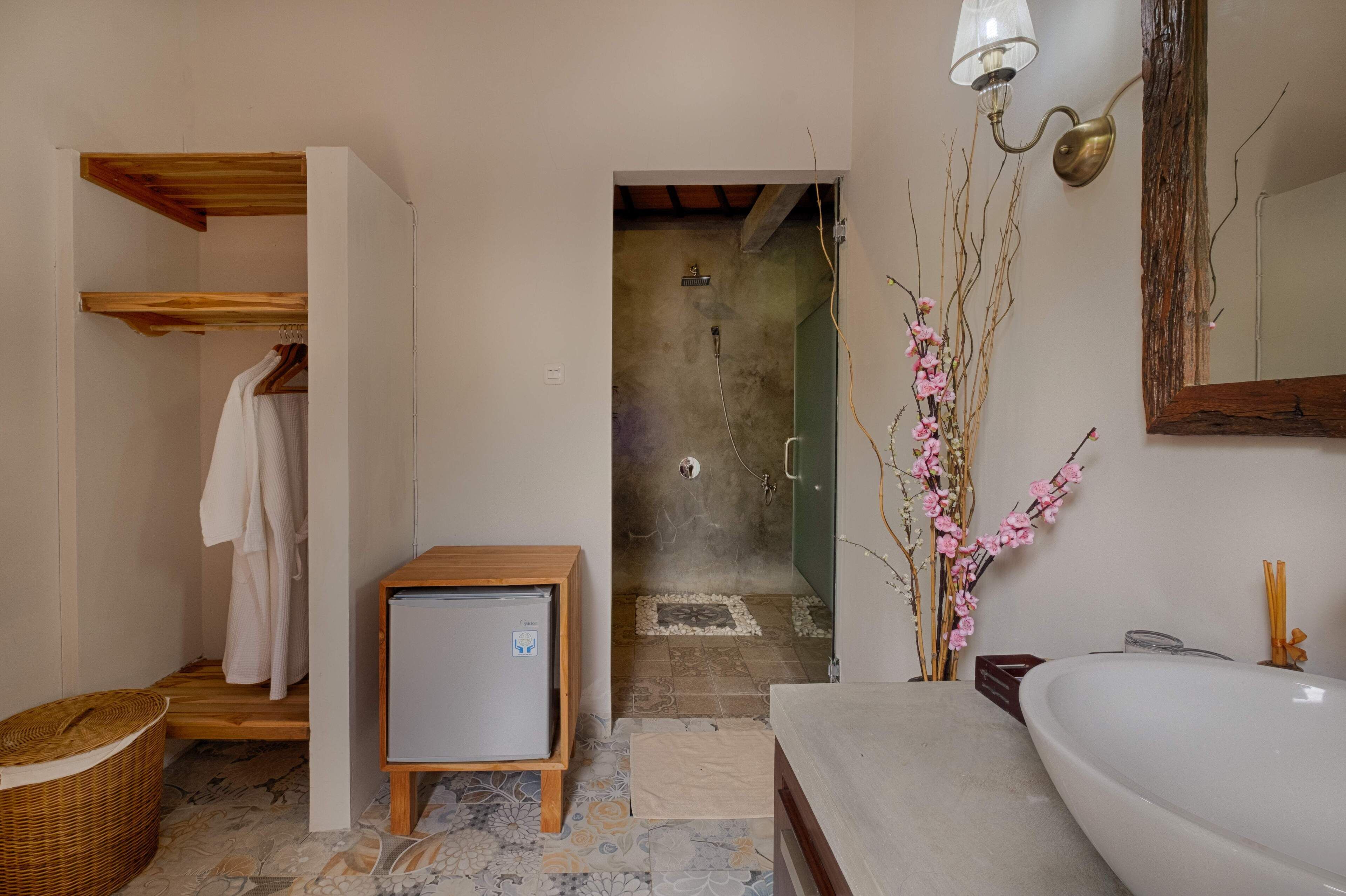Baño con ducha, lavamanos, toallero y un refrigerador pequeño.