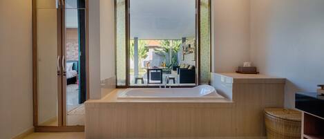 A modern bathroom with a large bathtub, a wooden vanity, and a view of an outdoor patio area.