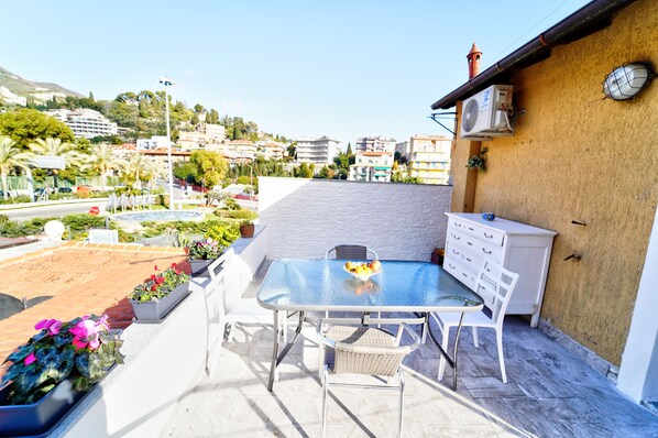 Una terraza en la azotea con una mesa, sillas, un aparador blanco y un reloj en la pared.