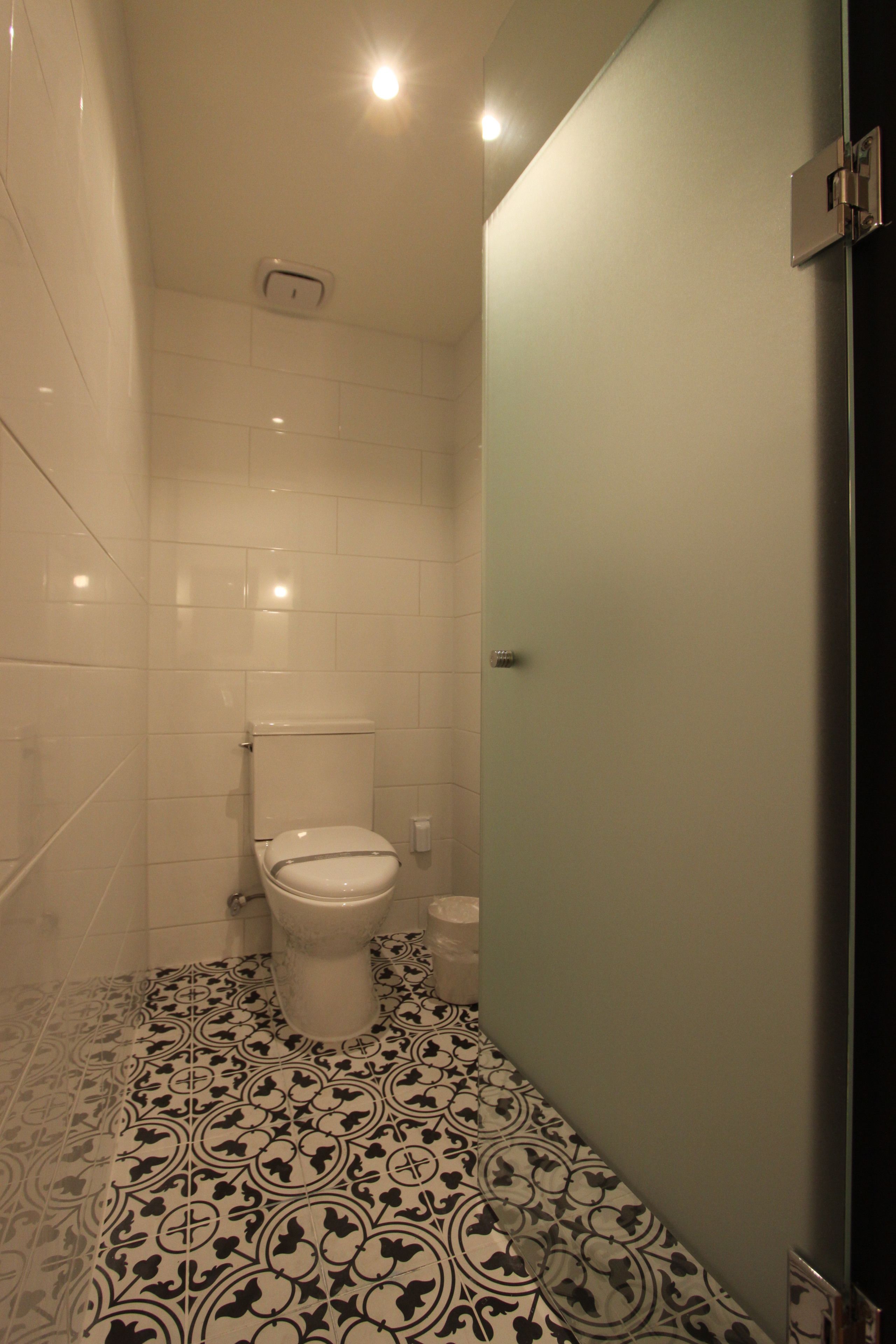 A bathroom with a toilet, a sink, and a mirror. The floor has a patterned tile design.