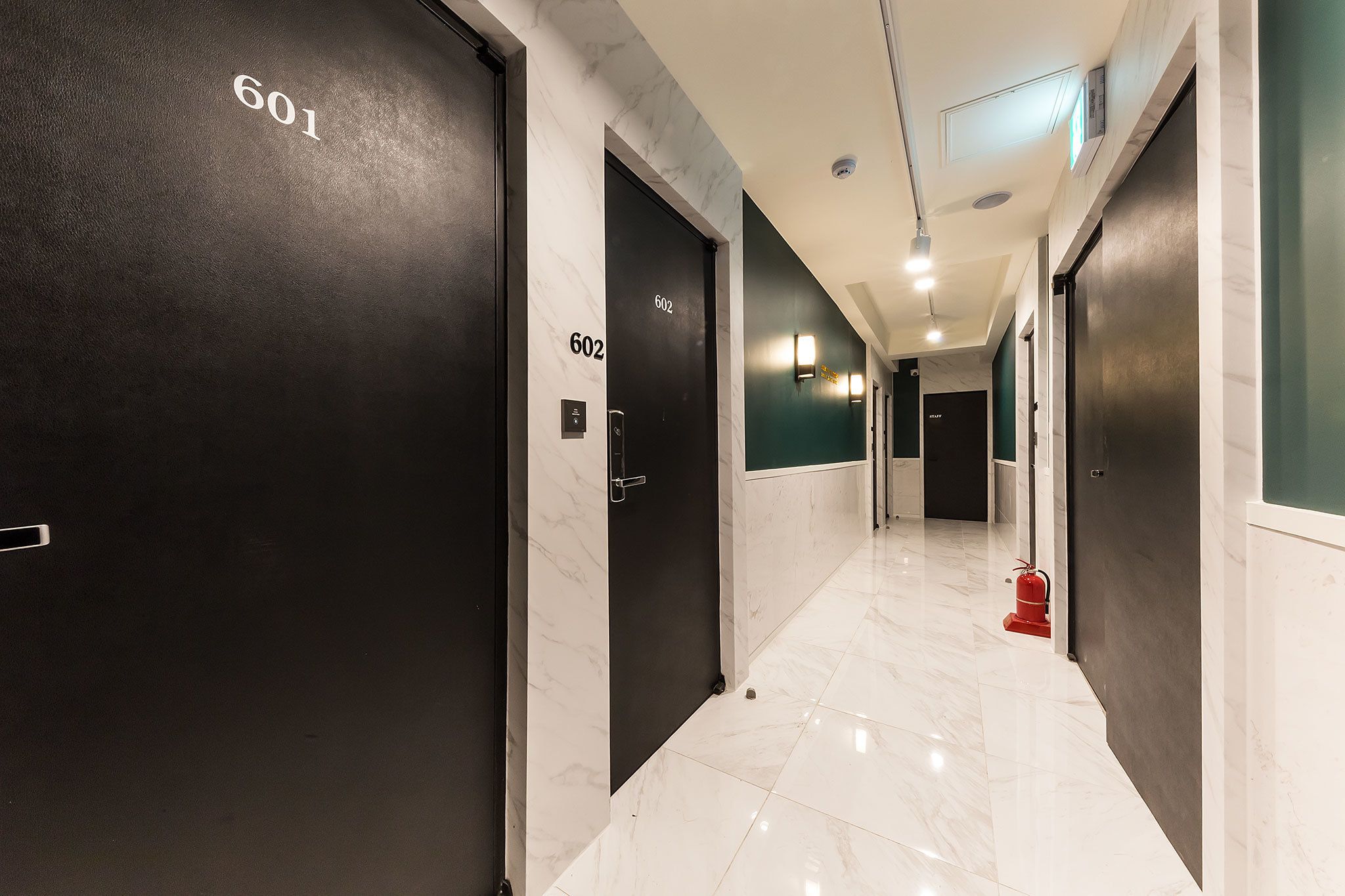 A hallway with black doors numbered 601 and 602, a red fire extinguisher, and a marble floor.