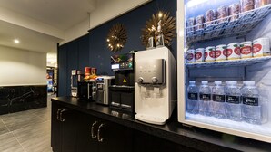 A hotel reception area with a water dispenser, coffee machine, and a refrigerator stocked with beverages.