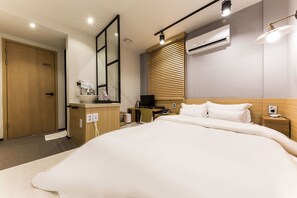 A modern hotel room with a large bed, a desk with a computer, a TV, and an air conditioning unit.