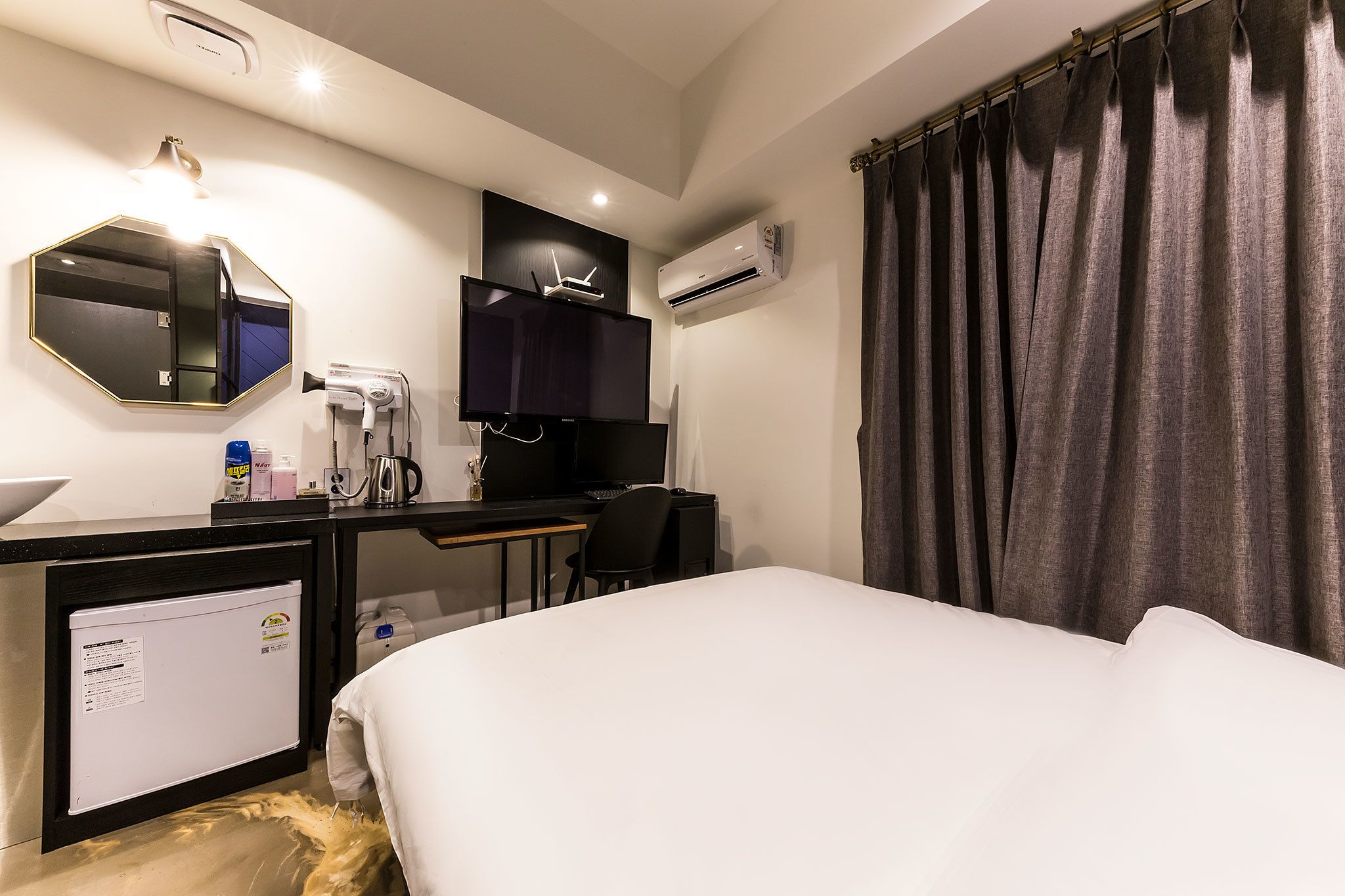 Ein Hotelzimmer mit Bett, Schreibtisch mit Computer, Spiegel, Klimaanlage und kleinem Kühlschrank.