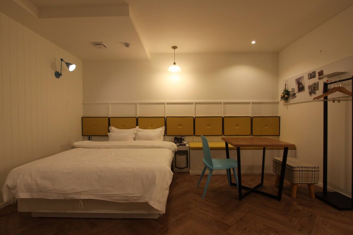 A bedroom with a bed, bedside table, lamp, chair, and a small table with a chair.