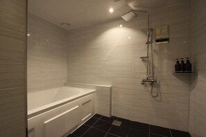 A modern bathroom with a white bathtub, a showerhead, and a small shelf with toiletries.