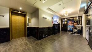 A hotel reception area with a marble reception desk, a wooden door labeled "JUNG," and a sign that reads "Who is looking for you?"