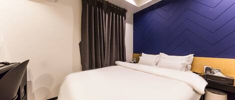 A hotel room with a bed, a desk, an air conditioner, a nightstand, and a lamp.