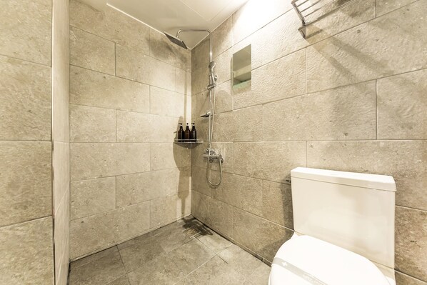 Un baño con azulejos color beige, ducha e inodoro.
