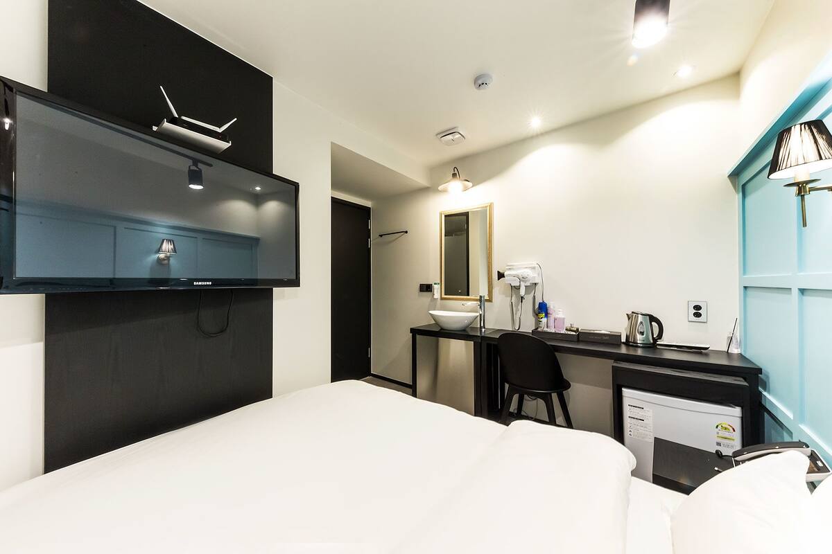 A modern hotel room with a bed, a desk with a sink, a mirror, and a television mounted on the wall.