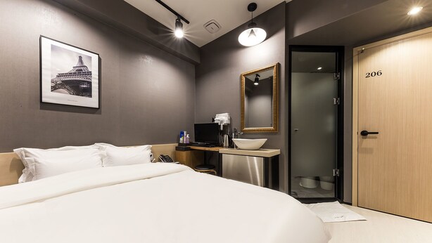 A hotel room with a large bed, a desk with a computer and a bowl, a mirror, and a door with the number 206.