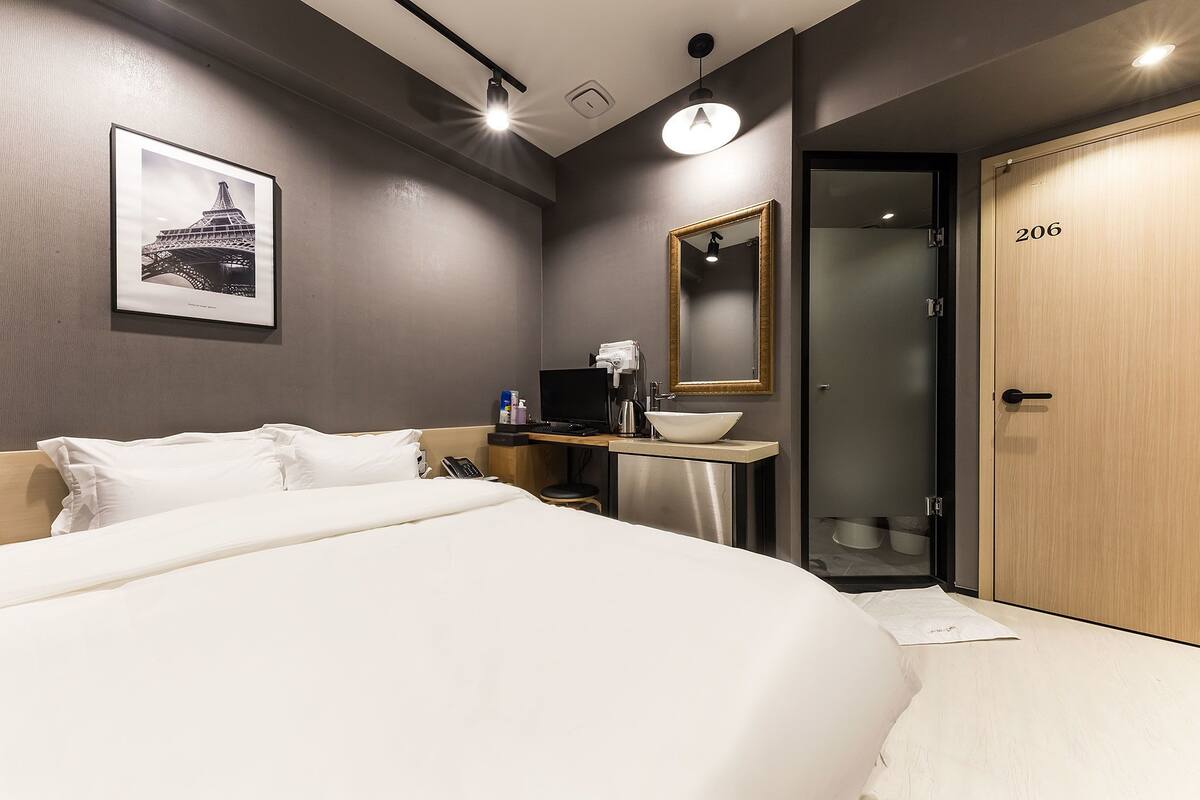 A hotel room with a large bed, a desk with a computer and a bowl, a mirror, and a door with the number 206.