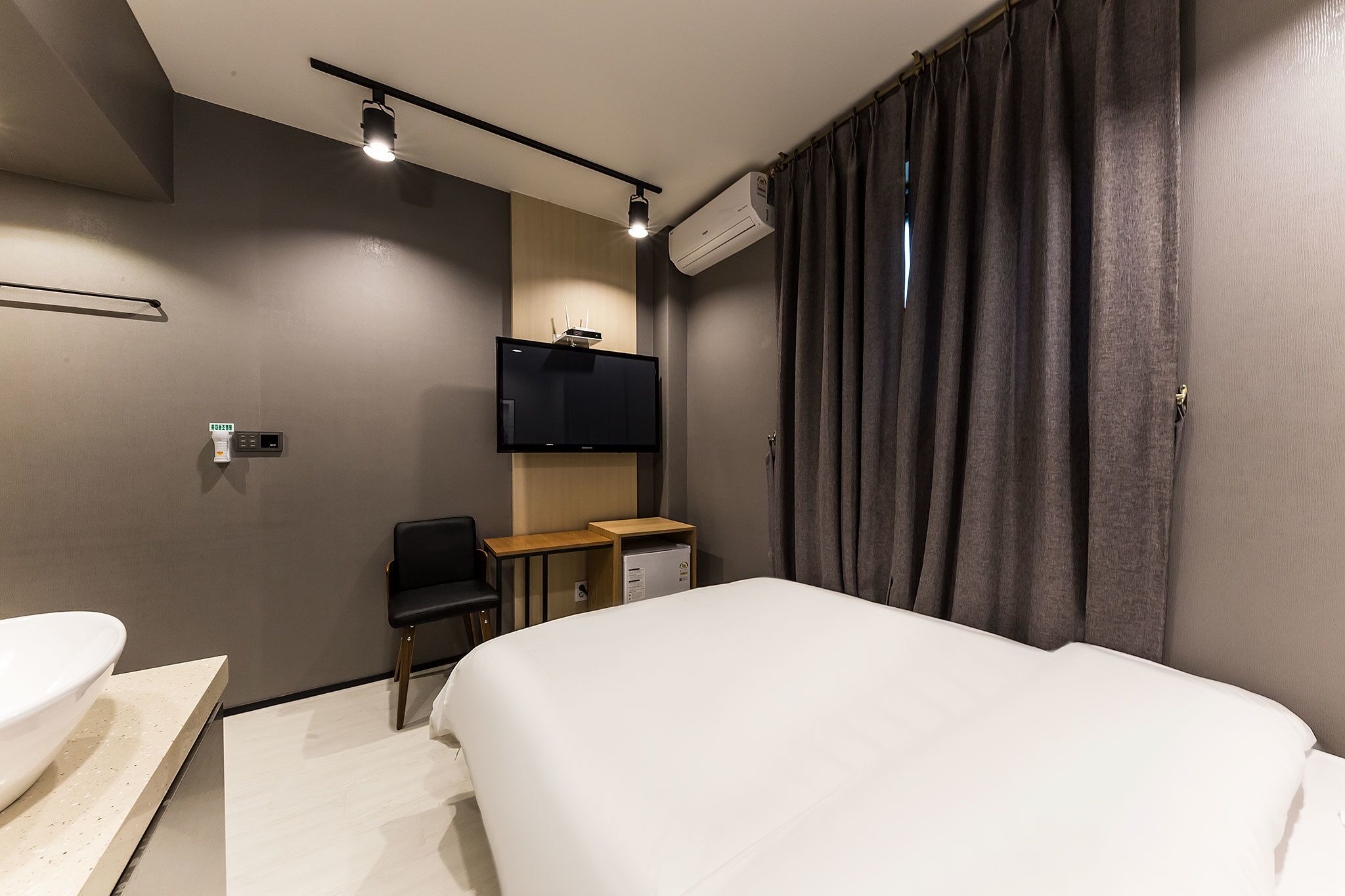 A hotel room with a bed, a desk, a chair, a TV, and an air conditioning unit.
