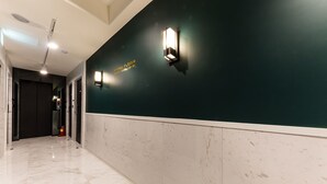 A hotel corridor with a dark green wall, white marble flooring, and two wall-mounted light fixtures.