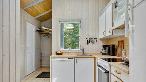 A compact kitchen with wooden cabinets, a built-in oven, and a window overlooking greenery. - Gorgeous home in Dronningmølle (Dronningmølle)