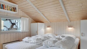 A bedroom with a wooden ceiling, a bed with white bedding, a window with curtains, and a bookshelf with books. - Gorgeous home in Dronningmølle (Dronningmølle)
