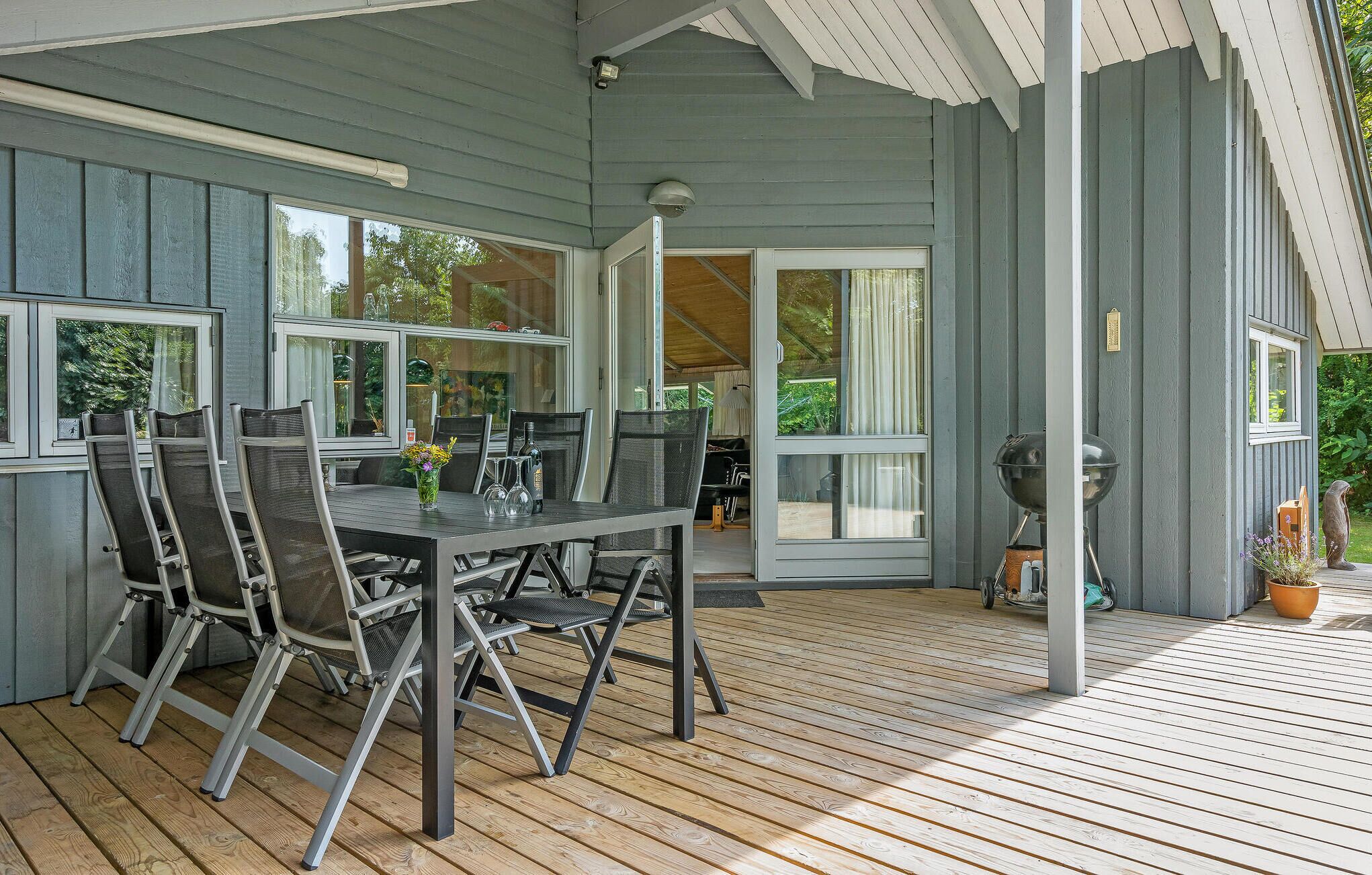 A covered outdoor area with a table and chairs, a grill, and a potted plant.