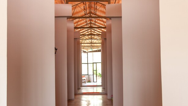 A corridor with a wooden ceiling and white walls, leading to a bright area with natural light.