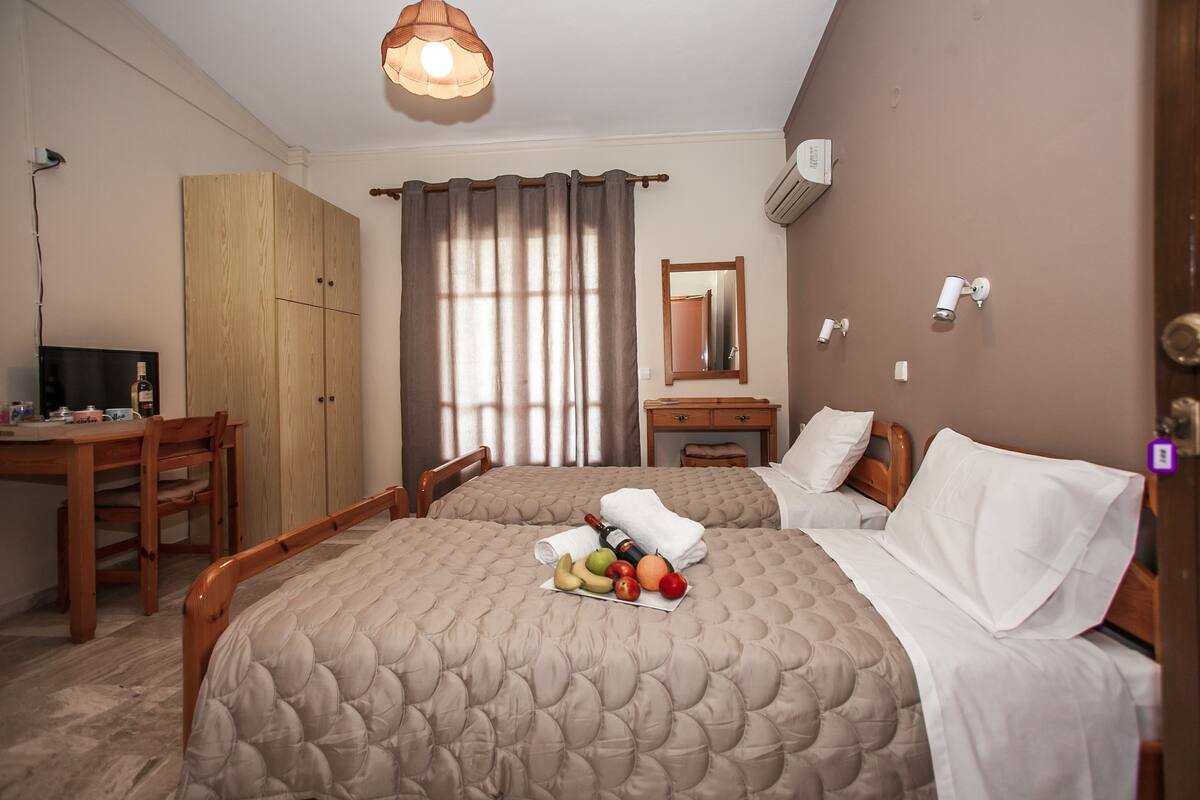 Ein Hotelzimmer mit zwei Betten, einem Holztisch, einem Stuhl, einem Spiegel und einer Obstschale auf dem Bett.