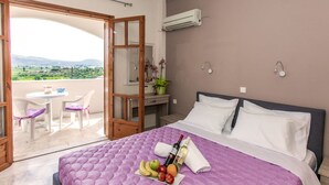 A bedroom with a large bed, a balcony with a table and chairs, and a view of the countryside.