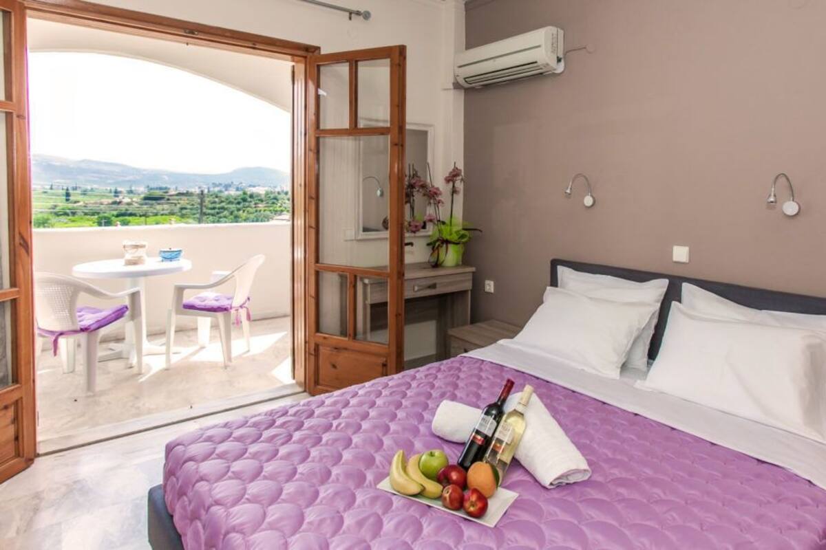 Ein Schlafzimmer mit einem großen Bett, einem Balkon mit Tisch und Stühlen und Blick ins Grüne.