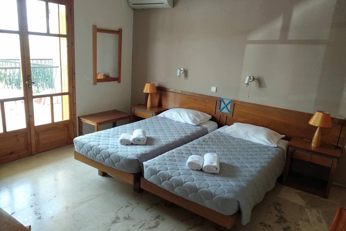 Ein Hotelzimmer mit zwei Betten, einem Holz-Kopfteil, Nachttischlampen, einem Spiegel und einer Klimaanlage.
