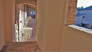 A narrow corridor with a table and chairs, leading to a room with a view of a building outside. - Contessa Ava Dei Lambardi - Hostel (Monteriggioni)