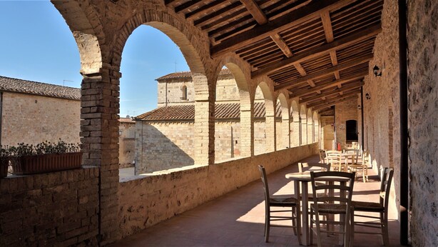 A covered outdoor area with stone arches, wooden tables, and chairs, suggesting a dining or relaxation space. - Contessa Ava Dei Lambardi - Hostel (Monteriggioni)