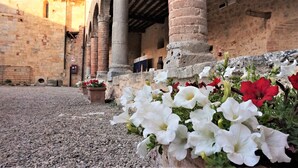 An outdoor courtyard with stone walls, columns, and flower planters with white and red flowers. - Contessa Ava Dei Lambardi - Hostel (Monteriggioni)