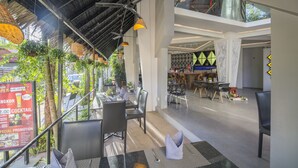 An indoor dining area with tables and chairs, a high ceiling with a woven design, hanging lights, and a view of the street outside. - Natural House (Siem Reap)