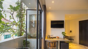 A modern hotel room with a balcony, a desk, a chair, a bed, and a TV. - Natural House (Siem Reap)